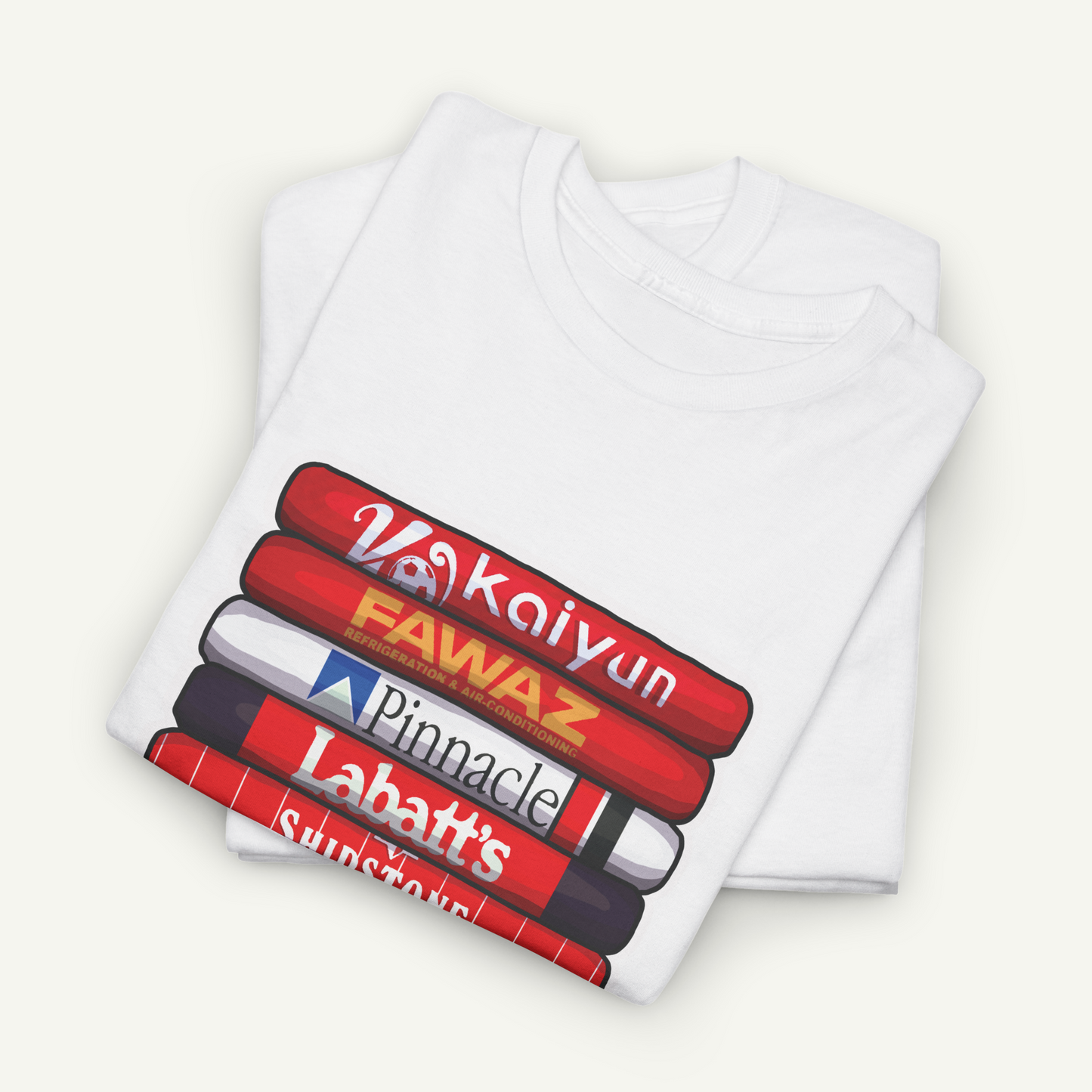 A white t-shirt with a graphic design depicting a stack of colorful books or magazines with the titles "Vakkoin", "Fawaz", "Pinnacle", "Labatt's", and "Sunnyside" printed on it.