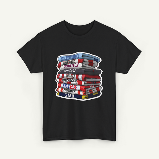A black t-shirt with a graphic design depicting a stack of colorful books or magazines with various titles such as "Hollywood", "Utilities", "Matchbook", "Heritage", and "GMK".