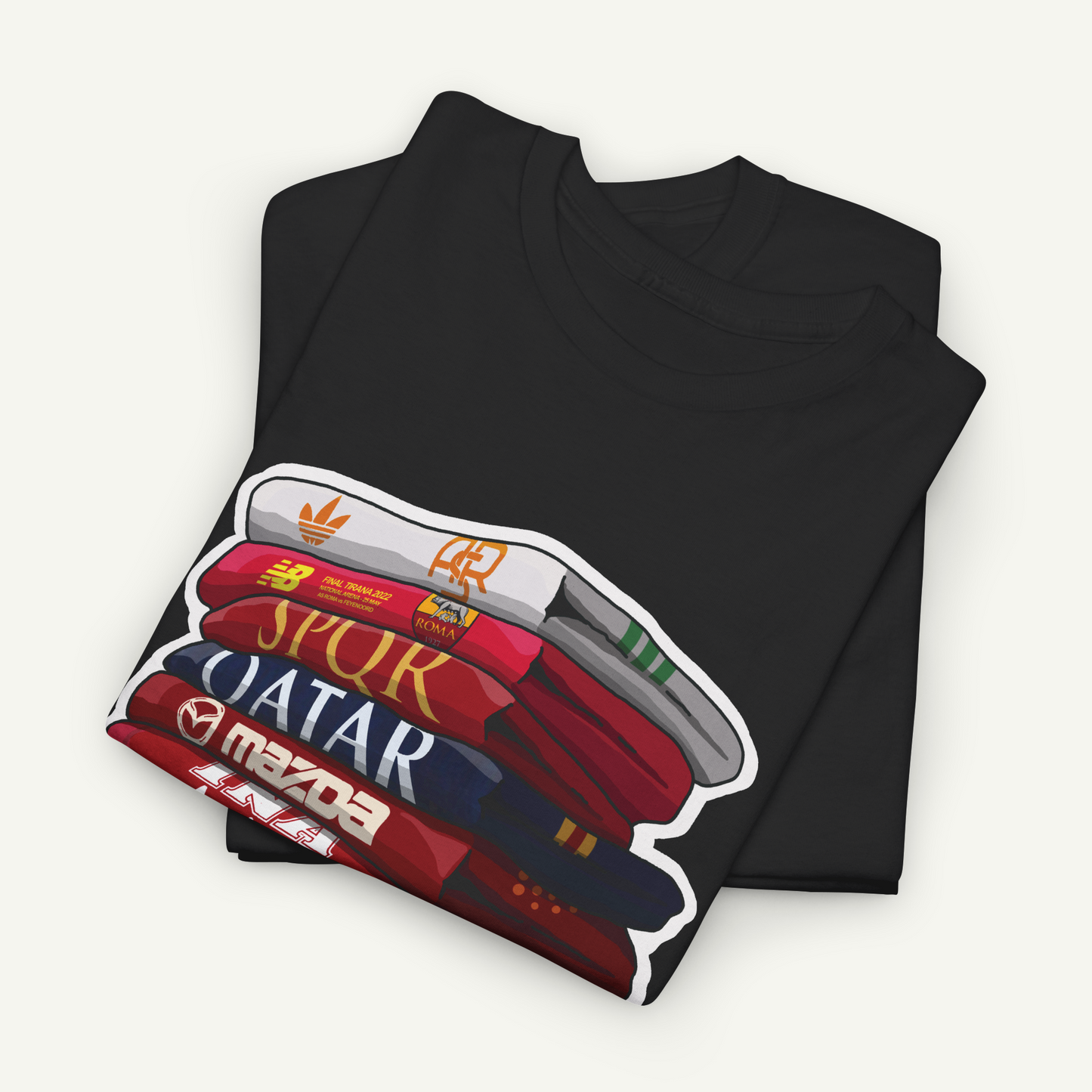 A black t-shirt with a graphic design depicting a stack of books or magazines with the titles "SPUR", "QATAR", and "MAZDA" printed on them.