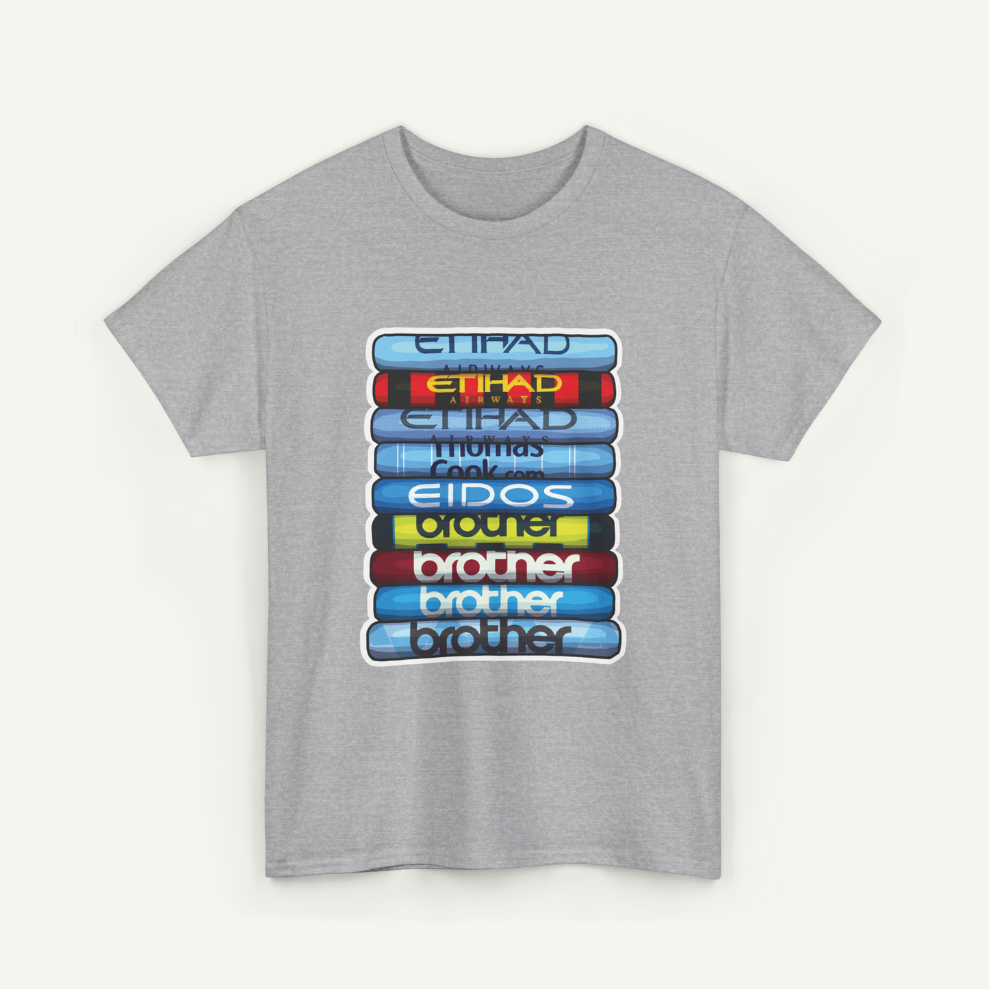 A gray t-shirt with a graphic design featuring a stack of colorful books or magazines with the titles "Etihad" and "Eidos" printed on them.