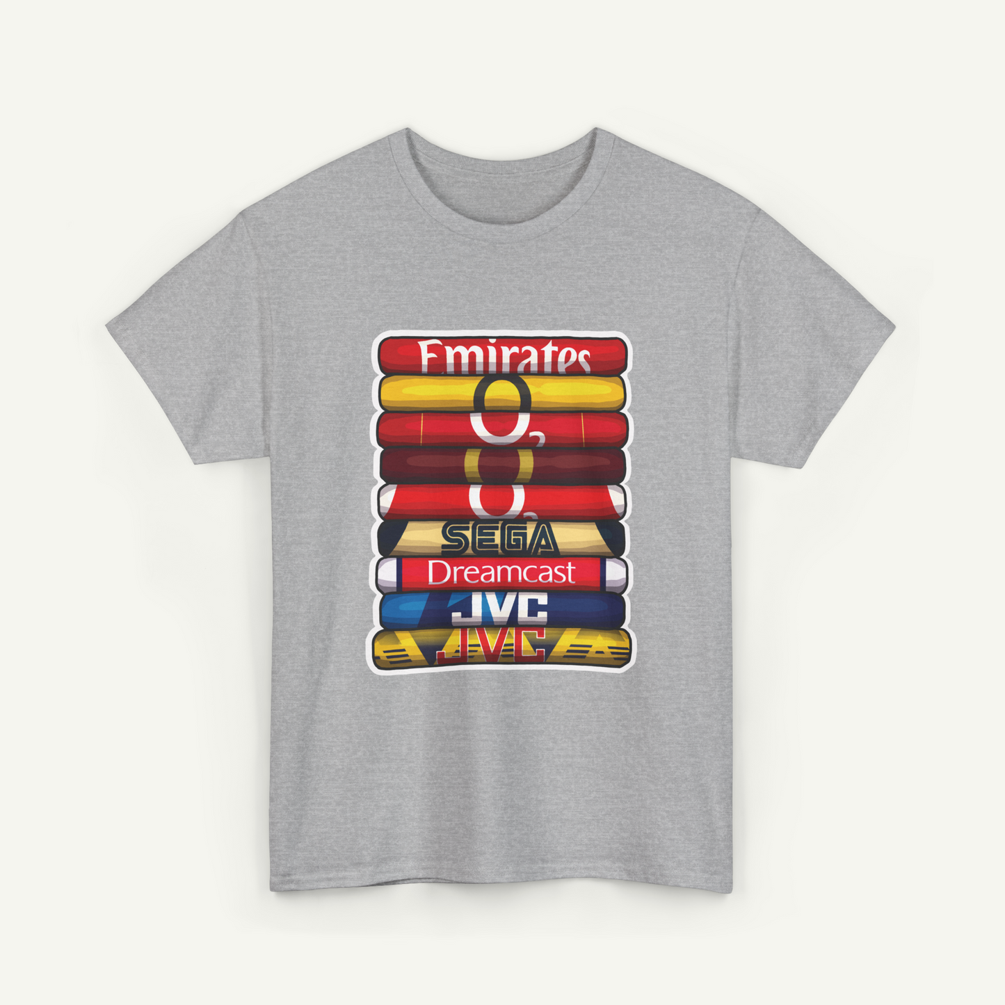 A gray t-shirt with a graphic design featuring a stack of colorful books or magazines with the text "Emirates", "SEGA Dreamcast", and "JVC" printed on them.