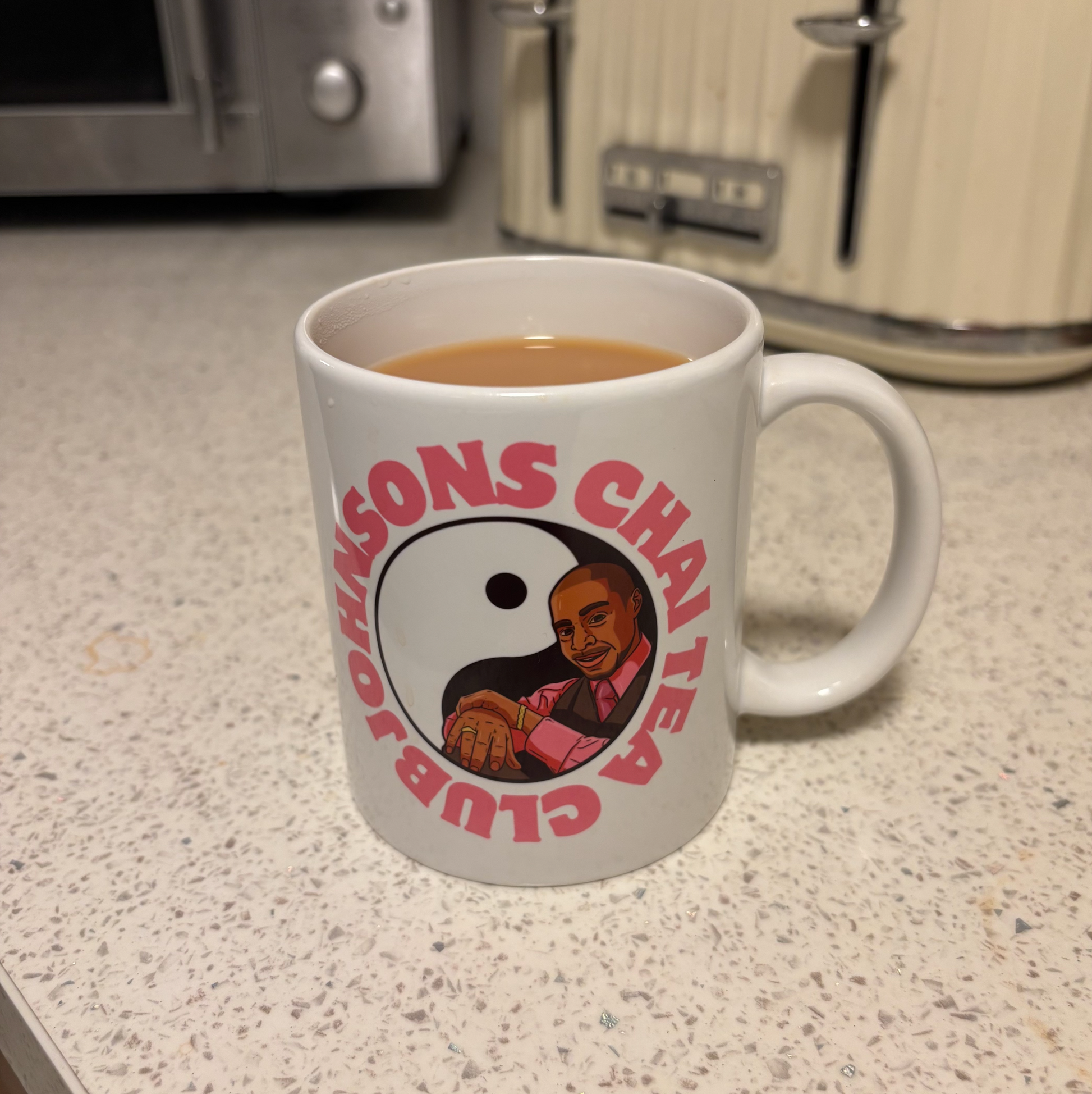 A white mug with a graphic design featuring a man's face and the text "JOHNSONS CHAI TEA CLUB" printed on it.