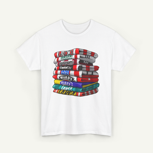 A white t-shirt with a colorful graphic design depicting a stack of various objects, including what appear to be books or magazines, with text labels on each item.