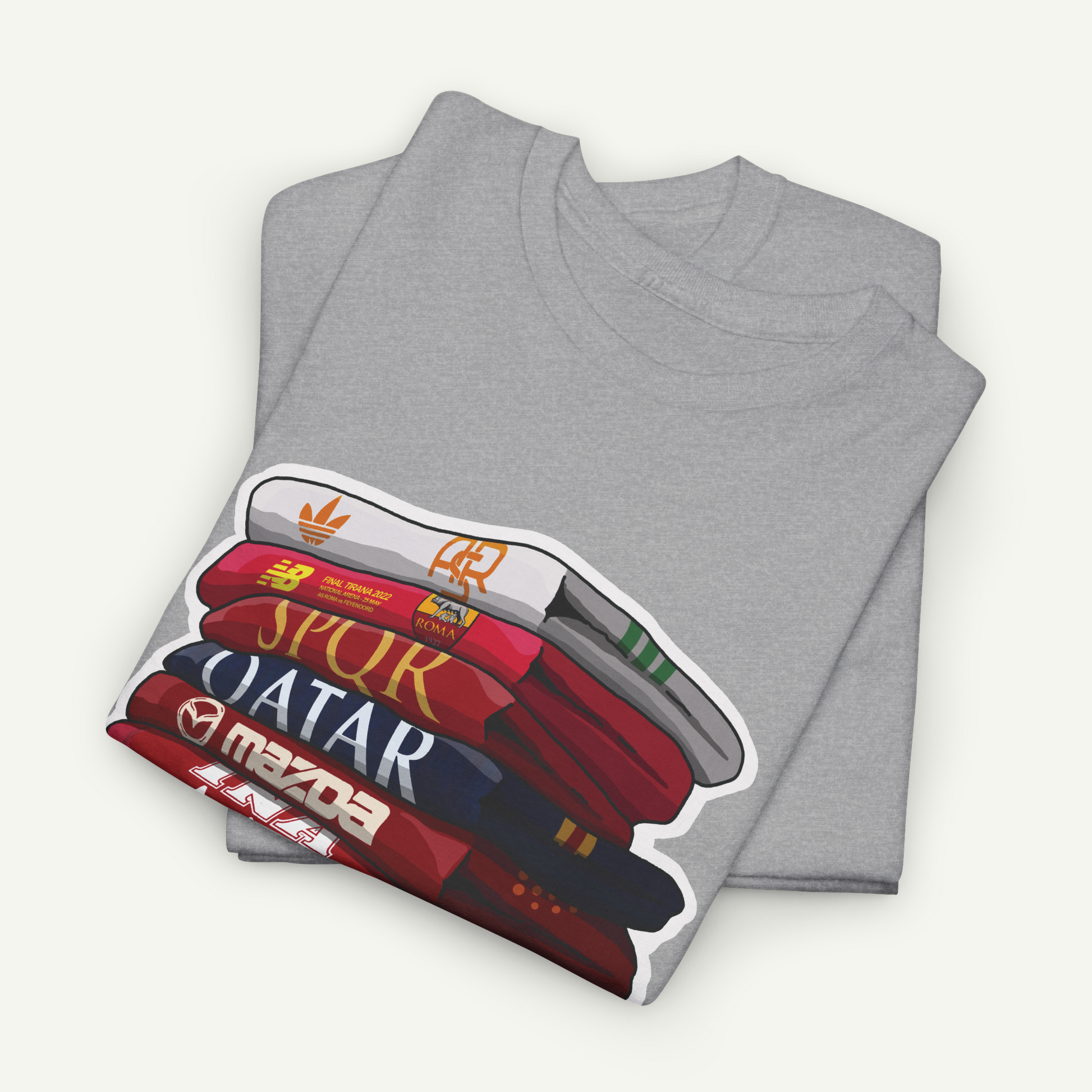 A gray t-shirt with a graphic design depicting a stack of books or magazines with the titles "SPUR", "QATAR", and "MAZDA" printed on them.