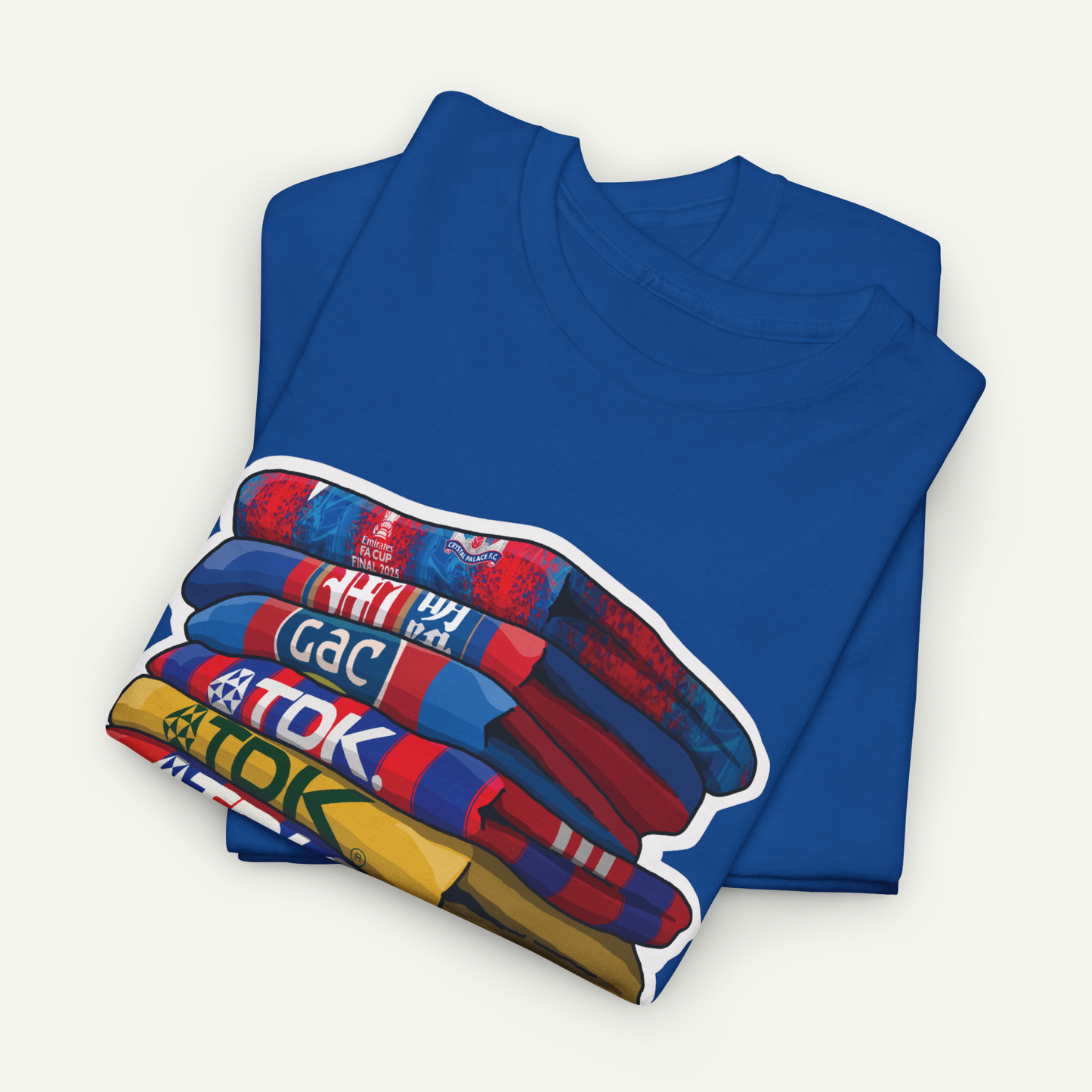 A blue t-shirt with a colorful graphic design depicting a stack of various colored objects, such as a blue and red striped scarf, a red and blue striped bag, and a blue and red striped towel.