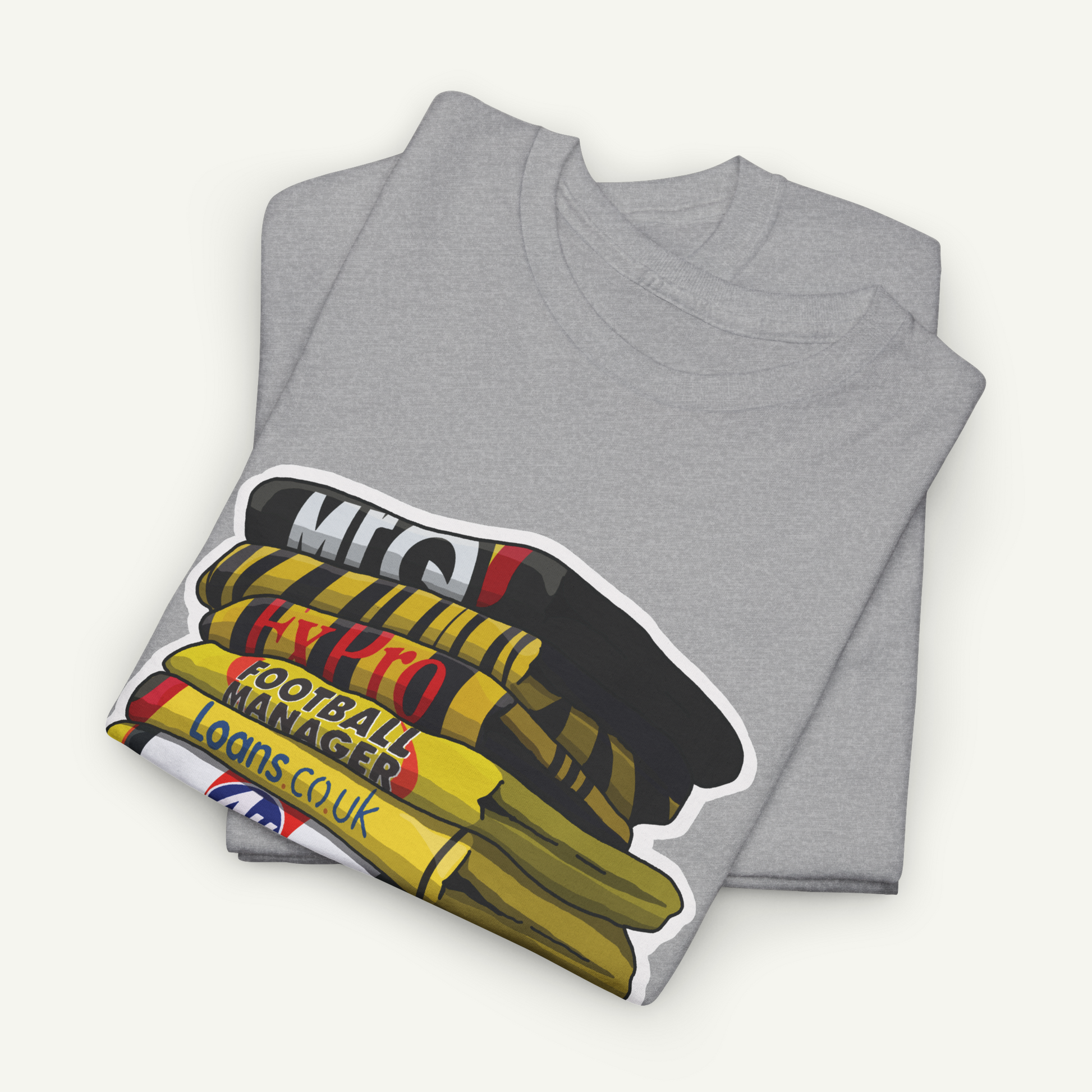 A gray t-shirt with a graphic design depicting a stack of books or magazines with the text "MEC" and "FOOTBALL MANAGER LOANS COU".