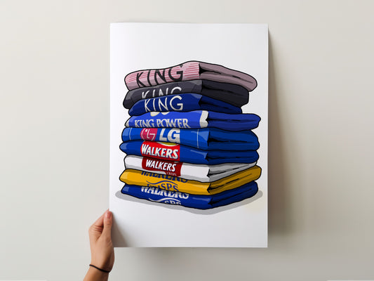 A hand is holding up a poster with a stack of colorful t-shirts on it.